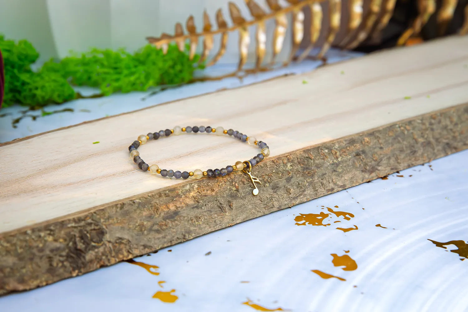 MELODIA MAGII - BRANSOLETKA Z LABRADORYTU I CYTRYNU, bransoletka z koralikami labradorytu i cytrynu, ułożona na drewnianym pomoście z zielonym mchem i złotymi liśćmi w tle.