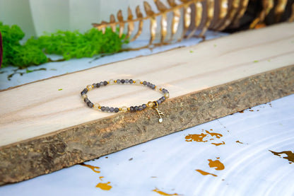 MELODIA MAGII - BRANSOLETKA Z LABRADORYTU I CYTRYNU, bransoletka z koralikami labradorytu i cytrynu, ułożona na drewnianym pomoście z zielonym mchem i złotymi liśćmi w tle.