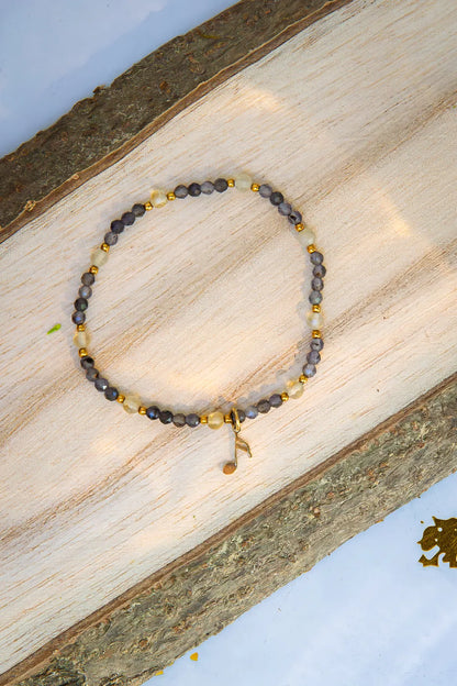 MELODIA MAGII - BRANSOLETKA Z LABRADORYTU I CYTRYNU, bransoletka z koralikami labradorytu i cytrynu, ułożona na drewnianym tle, z delikatnym złotym elementem.