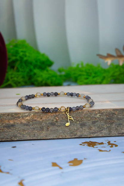 MELODIA MAGII - BRANSOLETKA Z LABRADORYTU I CYTRYNU, bransoletka z koralikami labradorytu i cytrynu, ułożona na drewnianym bloku z zielonym tłem.