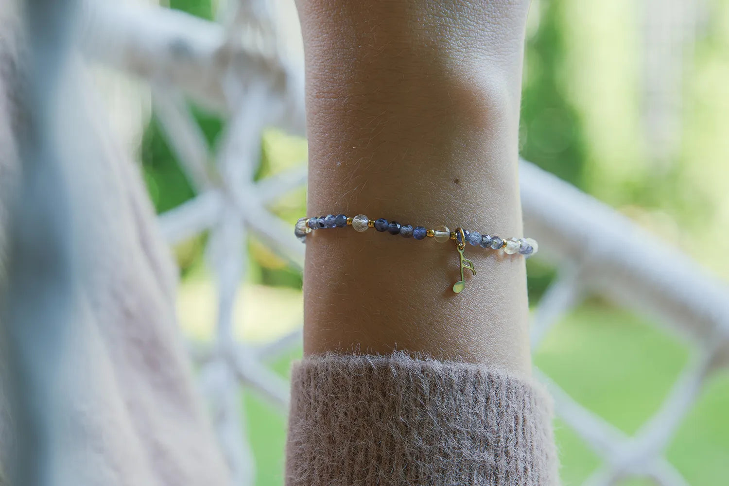 MELODIA MAGII - BRANSOLETKA Z LABRADORYTU I CYTRYNU na nadgarstku, z widocznymi niebieskimi kamieniami labradorytu i cytrynu, na tle białego ogrodzenia i zielonej roślinności.