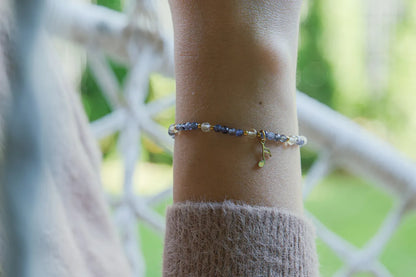 MELODIA MAGII - BRANSOLETKA Z LABRADORYTU I CYTRYNU na nadgarstku, z widocznymi niebieskimi kamieniami labradorytu i cytrynu, na tle białego ogrodzenia i zielonej roślinności.