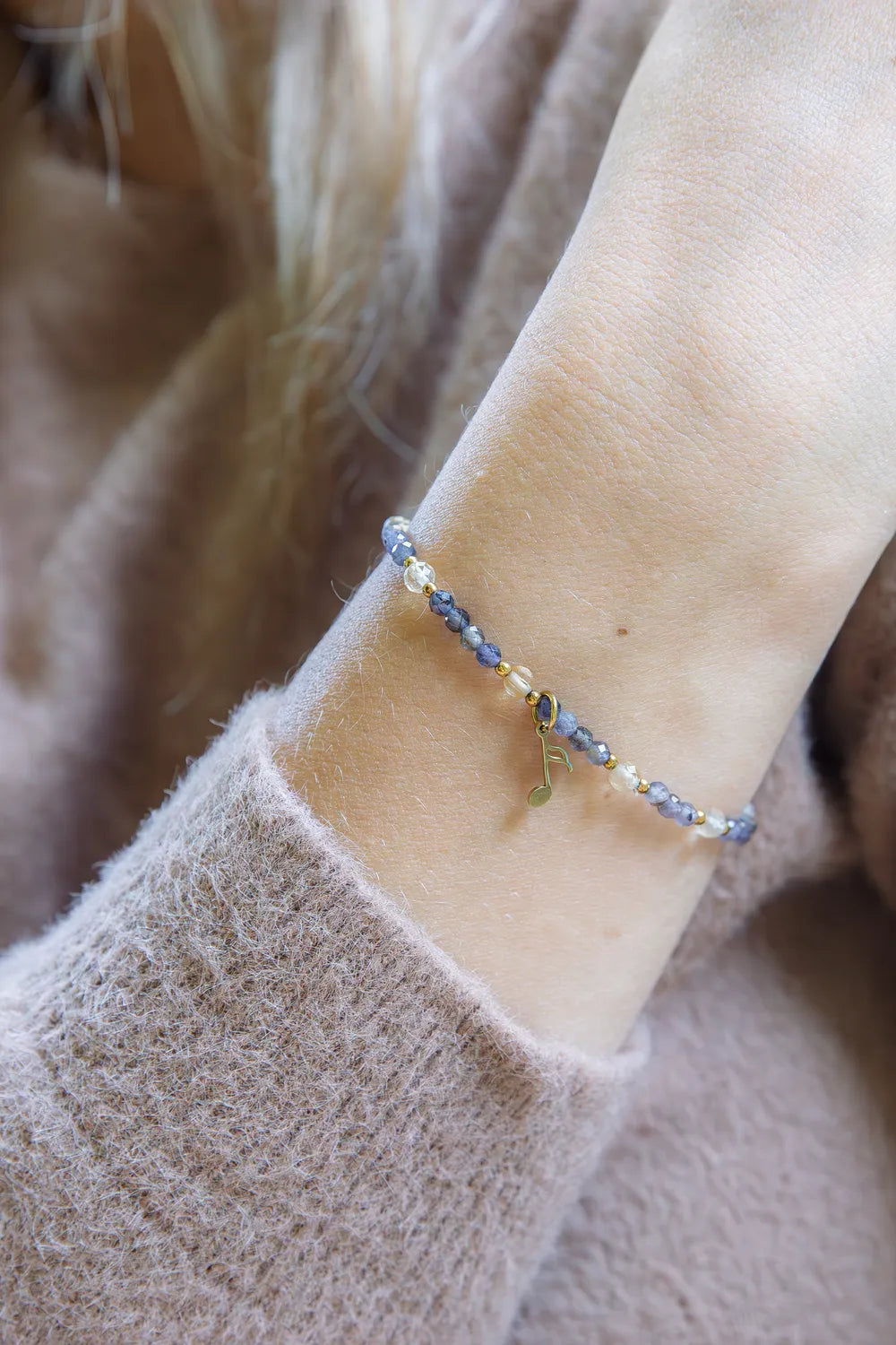 MELODIA MAGII - BRANSOLETKA Z LABRADORYTU I CYTRYNU na delikatnej dłoni, z widocznymi niebieskimi kamieniami labradorytu i cytrynu, na tle miękkiego, beżowego swetra.
