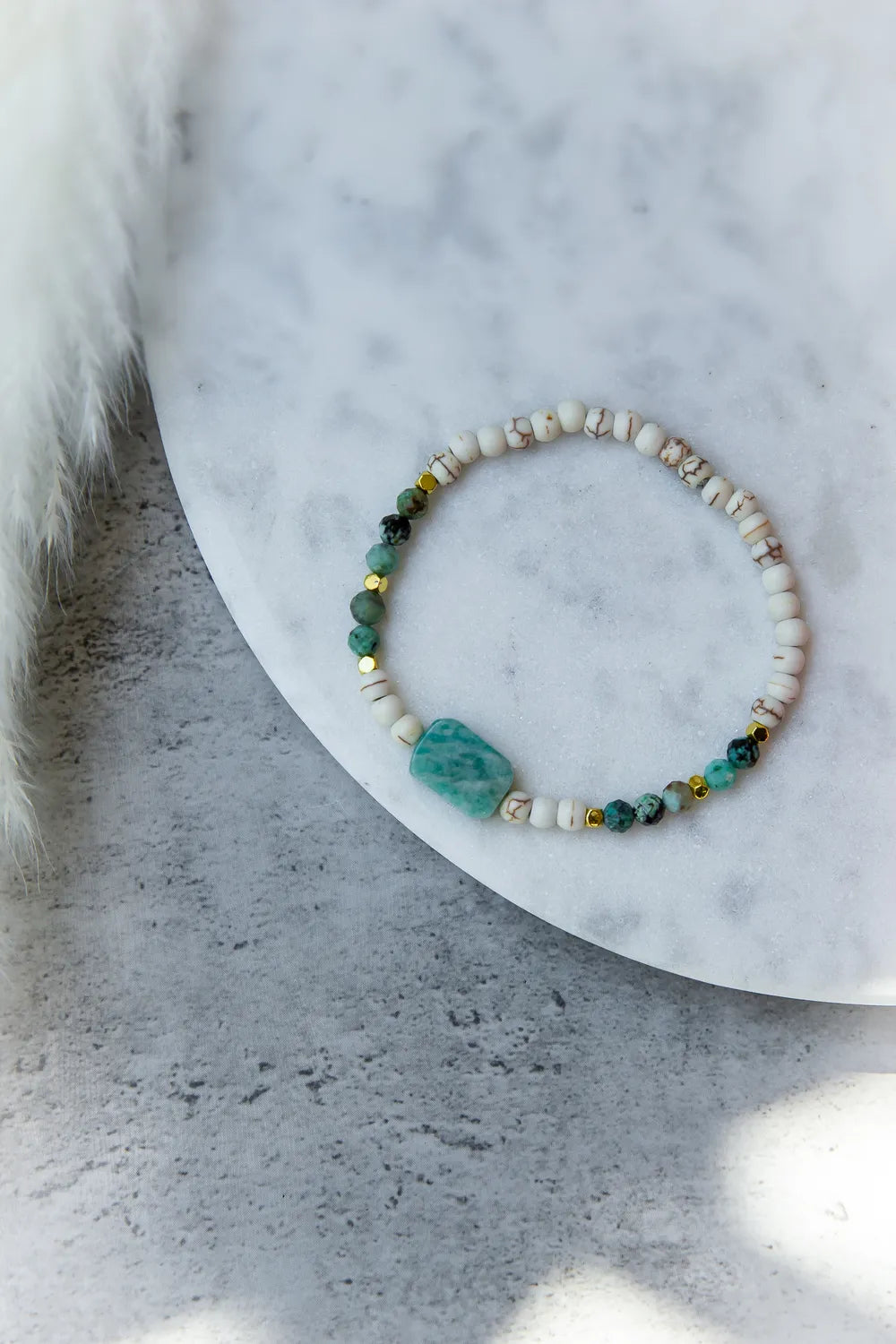 Morska Bryza Bransoletka Kamienie – Płasko ułożona, z akwamarynowym kamieniem centralnym i turkusowymi kuleczkami na białym tle.