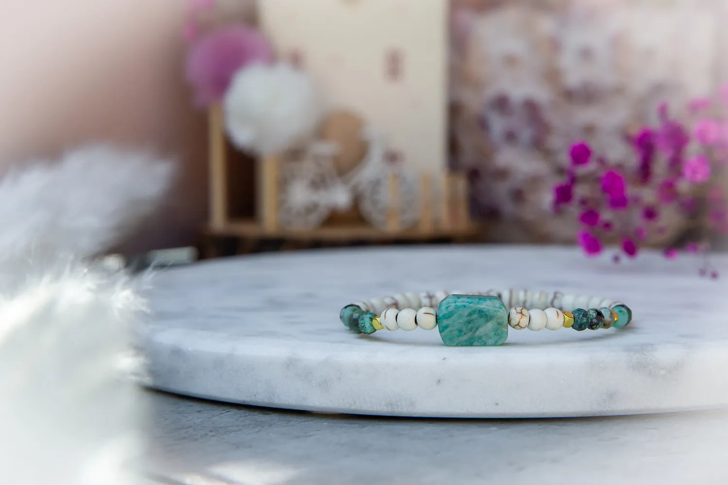 Morska Bryza Bransoletka Z Kamieniami z centralnym, turkusowym kamieniem, na białym marmurze z delikatnym, rozmazanym tłem.