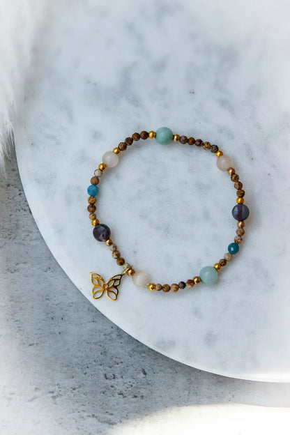 Motyli Taniec Bransoletka Z Kamieniami z motywem motyla, wykonana z kamieni w odcieniach brązu, błękitu i zieleni.