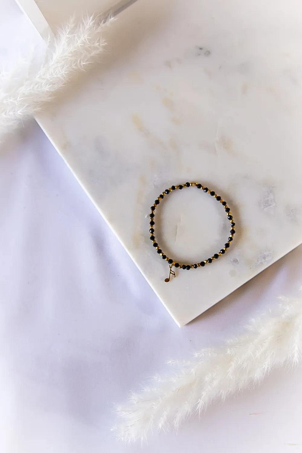 Muzyczna Nutka Bransoletka czarne Kamienie na białym marmurze, z subtelnym złotym zawężeniem i czarnymi kamieniami.