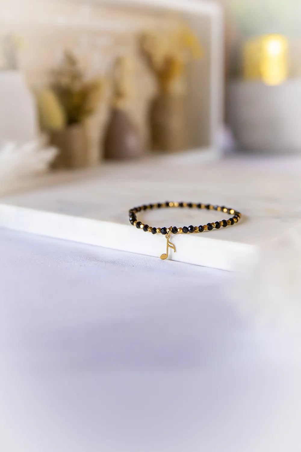 Muzyczna Nutka Bransoletka Dla Fana Muzyki Elegancka: czarna, koralikowa bransoletka z zawieszką w kształcie nutki na białym marmurze.