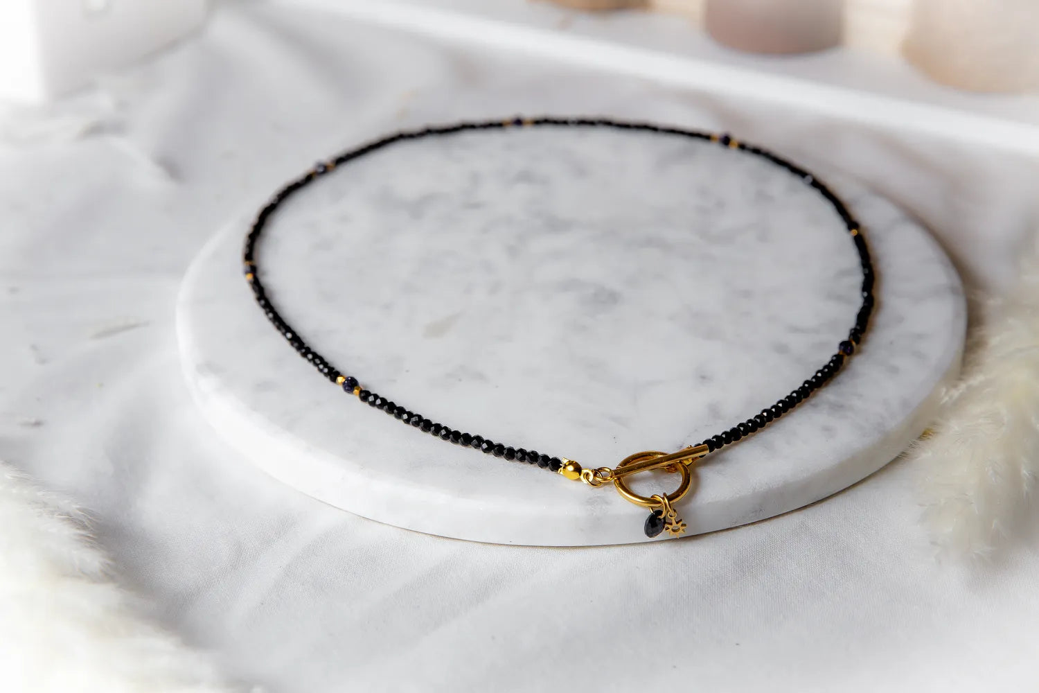 Noc Kairu Naszyjnik Czarny Koralik z złotym zapięciem toggle, ozdobiony drobnymi czarnymi fasetowanymi koralikami i złotymi akcentami.