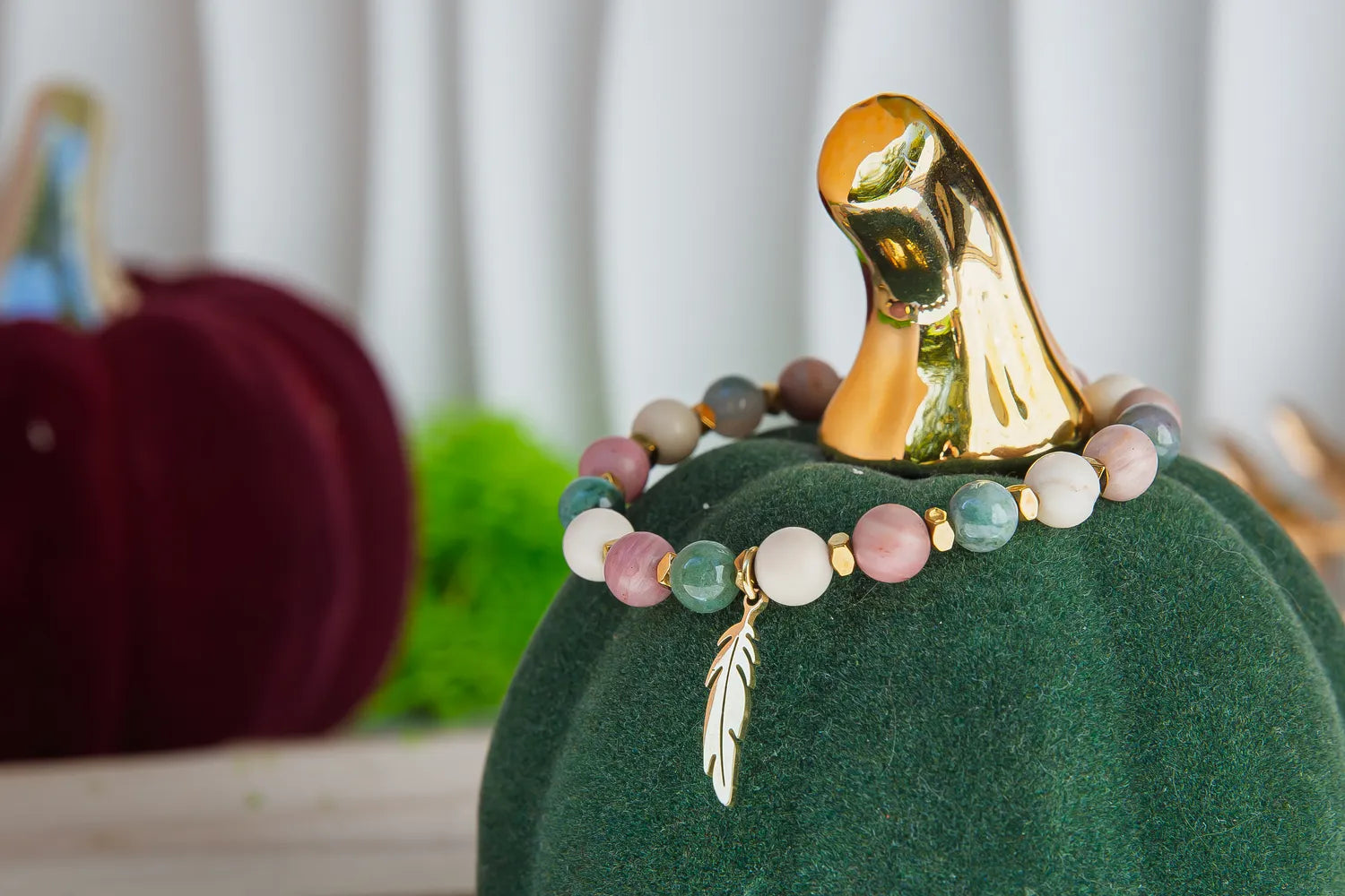 PAMIĘĆ ZIEMI - BRANSOLETKA Z KAMIENIA FOSYLNEGO, RODONITU I AGATU. Bransoletka z kolorowymi kamieniami i złotym liściem zawieszonym na zielonym dyniowym tle.
