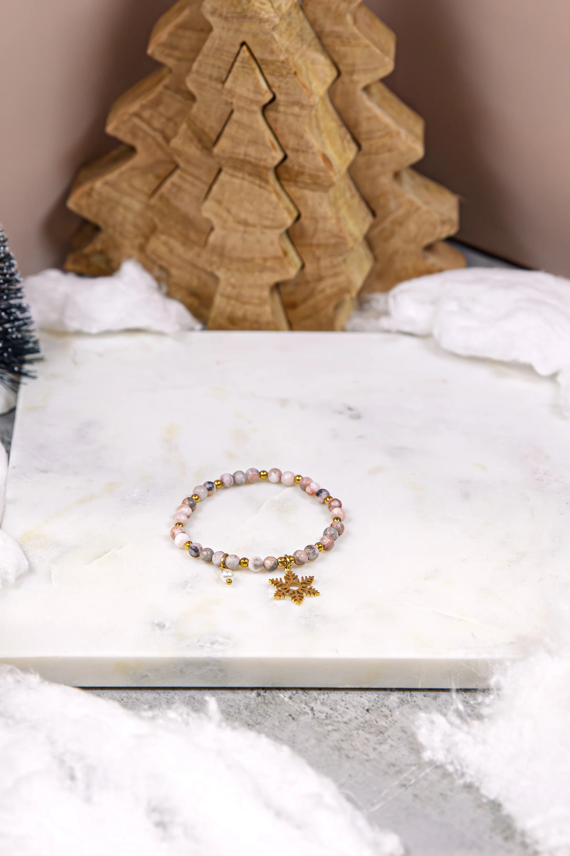 Zimowa bransoletka Pati Linka "Różany Szron" z naturalnego rodonitu i hematytu, ozdobiona złotą śnieżynką. Ręcznie robiony talizman w świątecznej aranżacji na marmurze.