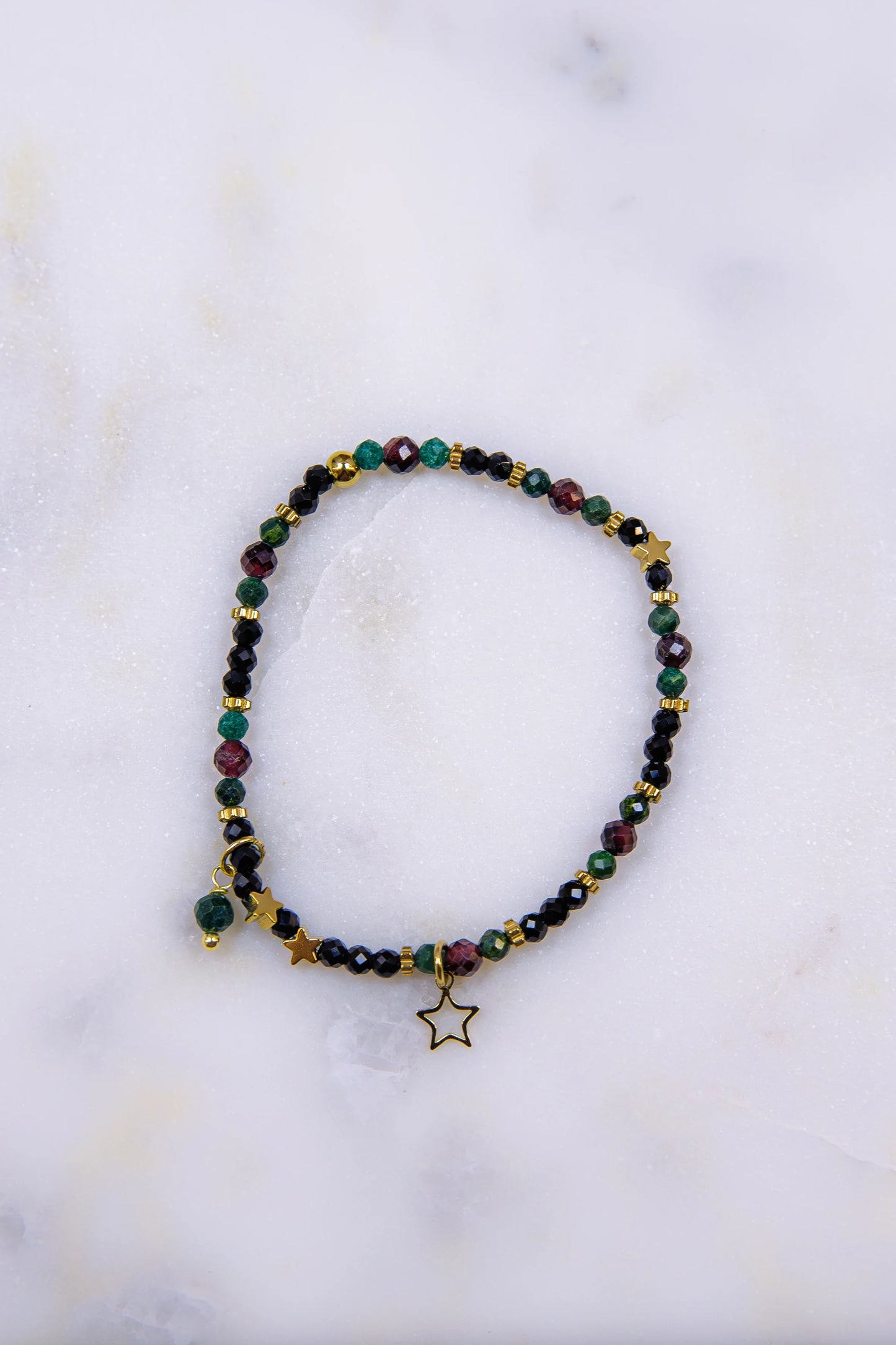 Zbliżenie (makro) na detale bransoletki: pozłacana zawieszka gwiazda oraz fasetowane kamienie naturalne – błyszczący czarny spinel i głęboki czerwony granat.