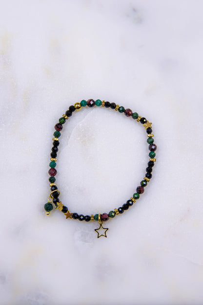 Zbliżenie (makro) na detale bransoletki: pozłacana zawieszka gwiazda oraz fasetowane kamienie naturalne – błyszczący czarny spinel i głęboki czerwony granat.