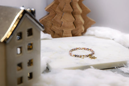 Zbliżenie na pozłacaną zawieszkę w kształcie śnieżynki i drobną kropelkę masy perłowej w bransoletce Pati Linka. Widoczne detale ręcznego rzemiosła.