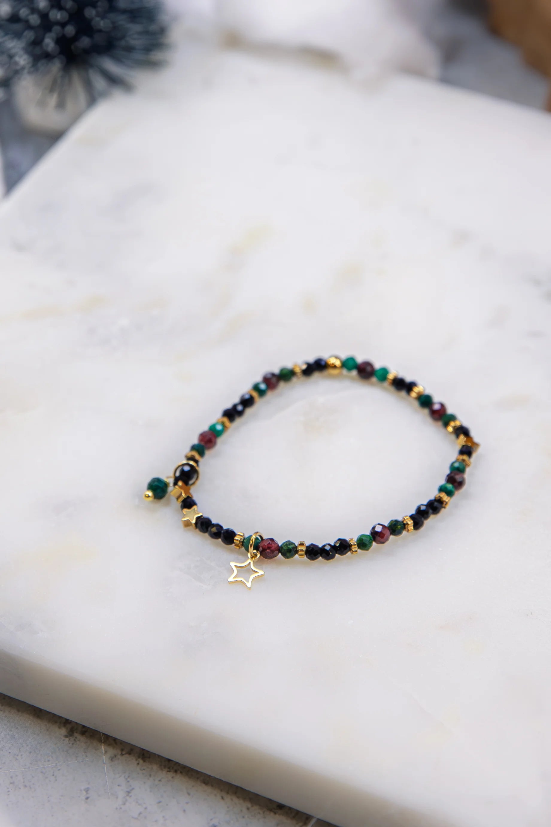 Widok z góry na elastyczną bransoletkę na gumce. Widoczny wzór ułożenia zielonych, czerwonych i czarnych kamieni przeplatanych drobnymi gwiazdkami z hematytu.