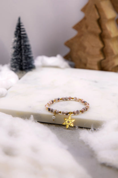 Bransoletka z rodonitu jako inspiracja na prezent świąteczny dla świadomej kobiety. Biżuteria talizman w otoczeniu zimowych dekoracji i sztucznego śniegu.