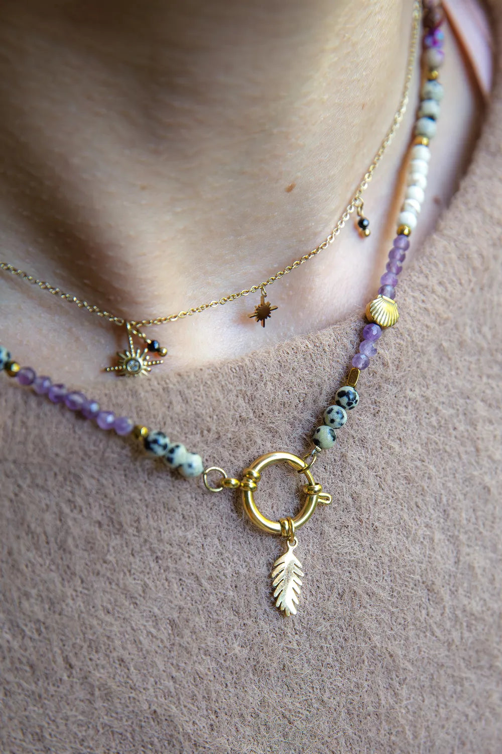 PEŁNIA HARMONII - NASZYJNIK Z AMETYSTU, HOWLITU I JASPISU DALMATYŃSKIEGO. Naszyjnik z kolorowymi kamieniami, w tym ametystem, howlitem i jaspisem dalmatyńskim, na delikatnej łańcuszku. Tło z beżowej tkaniny, ułożenie na szyi.