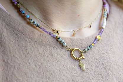 PEŁNIA HARMONII - NASZYJNIK Z AMETYSTU, HOWLITU I JASPISU DALMATYŃSKIEGO. Naszyjnik z kolorowymi kamieniami ametystu, howlitu i jaspisu dalmatyńskiego, ułożony na delikatnej skórze. Tło z beżowej tkaniny.