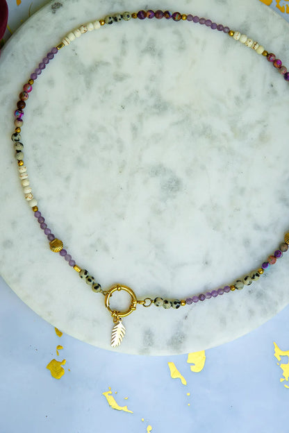 PEŁNIA HARMONII - NASZYJNIK Z AMETYSTU, HOWLITU I JASPISU DALMATYŃSKIEGO. Naszyjnik z kolorowymi kamieniami ametystu, howlitu i jaspisu dalmatyńskiego, ułożony na marmurowym tle z dodatkiem złotego liścia.