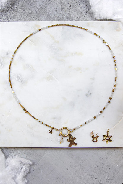 Naszyjnik z główną zawieszką w kształcie ludzika z piernika. Obok leżą dodatkowe, złote charmsy do wyboru: głowa renifera i śnieżynka. Biżuteria celebrująca indywidualność.