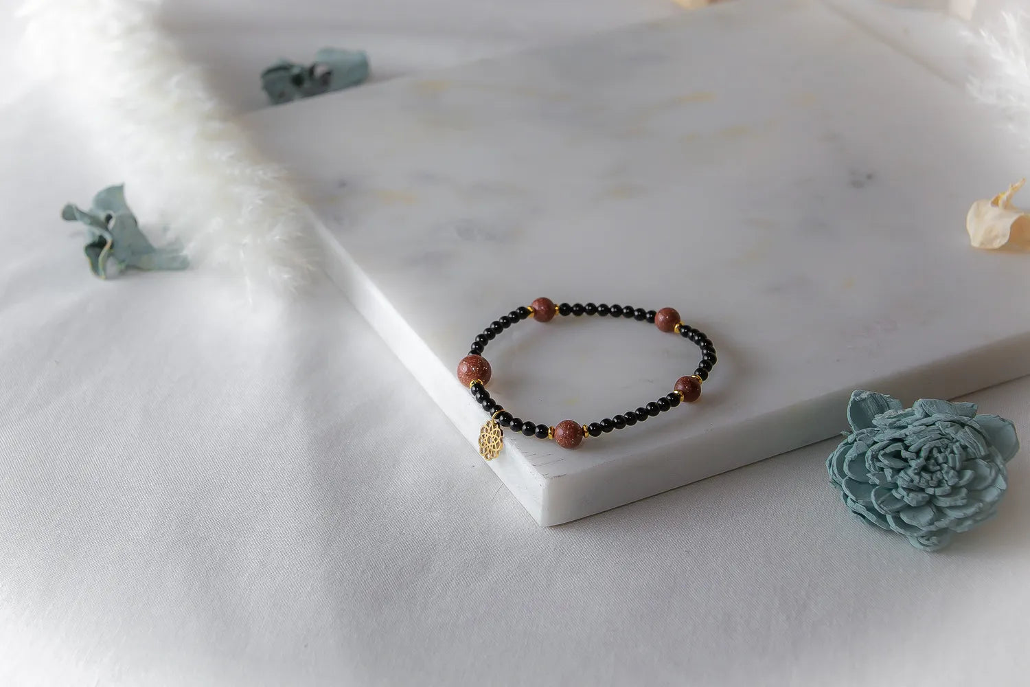 Pustynna Elegancja Bransoletka Piasku Pustyni na marmurowej desce z ozdobnymi kwiatami, czarne i złociste koraliki, złota zawieszka.