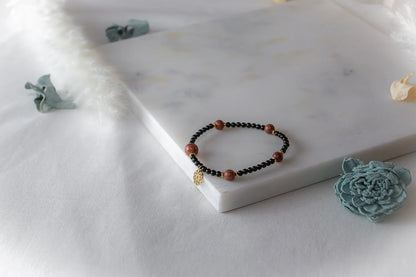 Pustynna Elegancja Bransoletka Piasku Pustyni na marmurowej desce z ozdobnymi kwiatami, czarne i złociste koraliki, złota zawieszka.