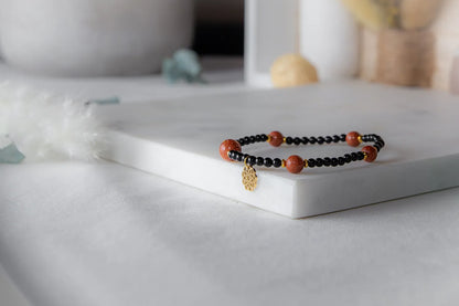 Pustynna Elegancja Bransoletka Piasku Pustyni: czarna, na białym tle, z piaskiem pustyni i złotym zawieszeniem.