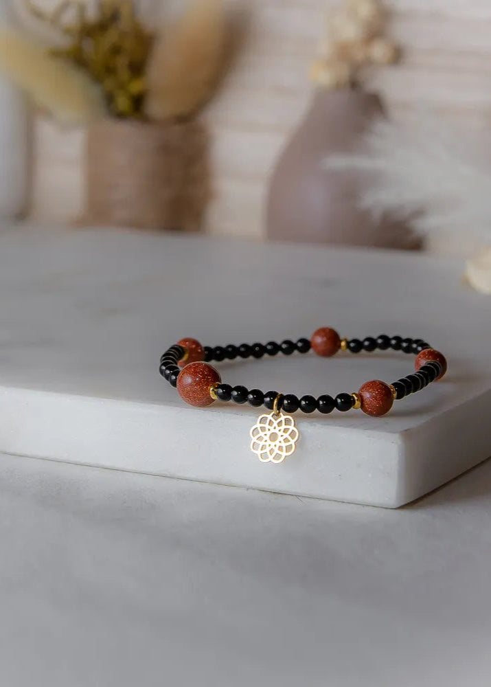 Pustynna Elegancja Bransoletka Z Piasku Pustyni z błyszczącymi, złotymi kamieniami piaskowymi i czarnymi koralikami, z zawieszką w kształcie mandali.