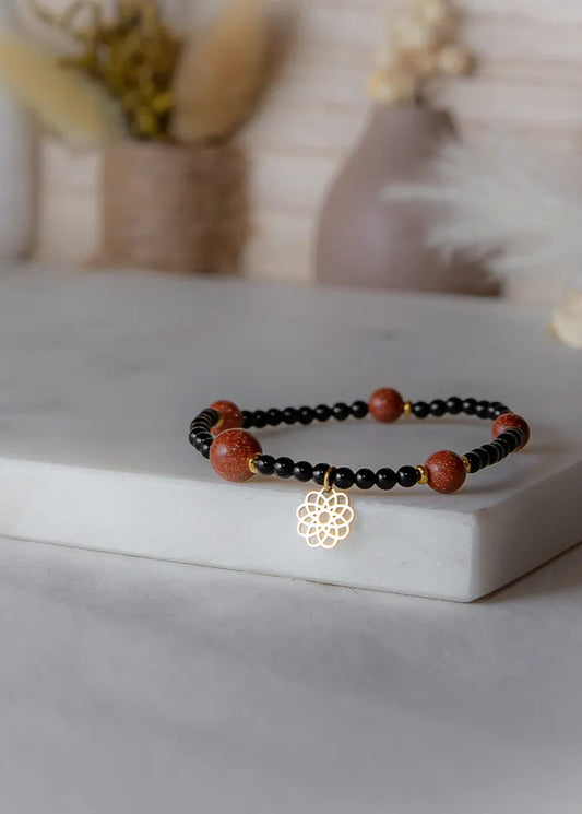 Pustynna Elegancja Bransoletka Z Piasku Pustyni z błyszczącymi, złotymi kamieniami piaskowymi i czarnymi koralikami, z zawieszką w kształcie mandali.