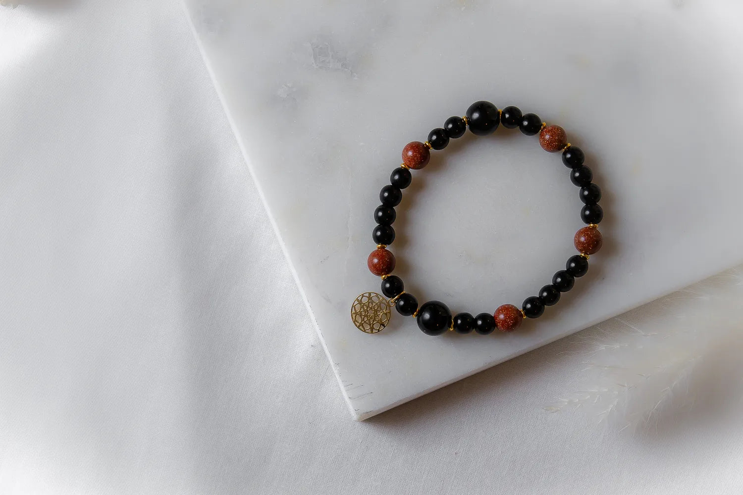 Pustynna Moc Bransoletka XL Piask Pustyni Onyks na marmurowej płytce z białym tłem, ozdobiona złotym medalionem.