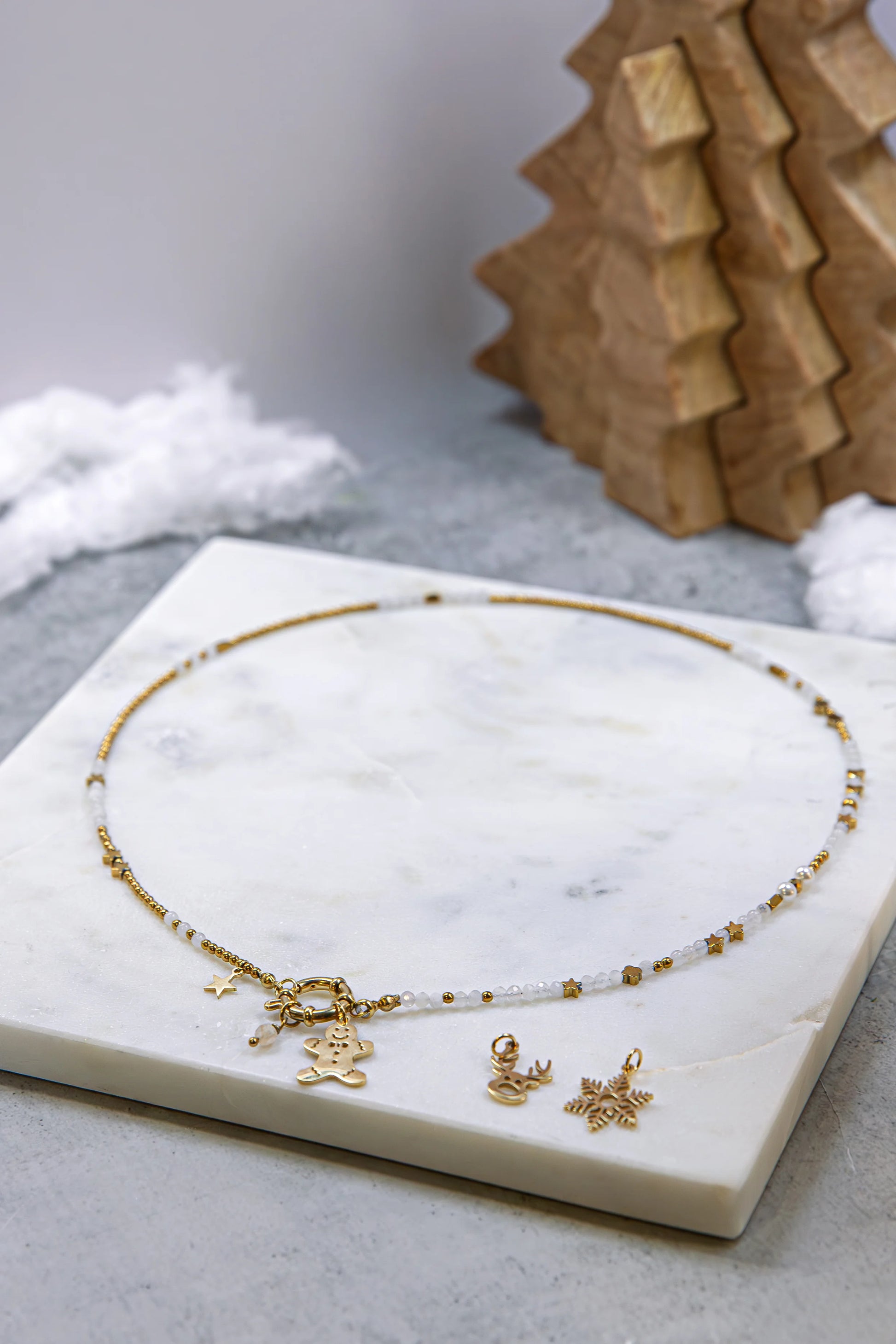 Delikatny, ręcznie robiony naszyjnik na złotym łańcuszku z drobnymi koralikami. Widoczne detale złotych zawieszek: ludzik z piernika, głowa renifera i płatek śniegu.