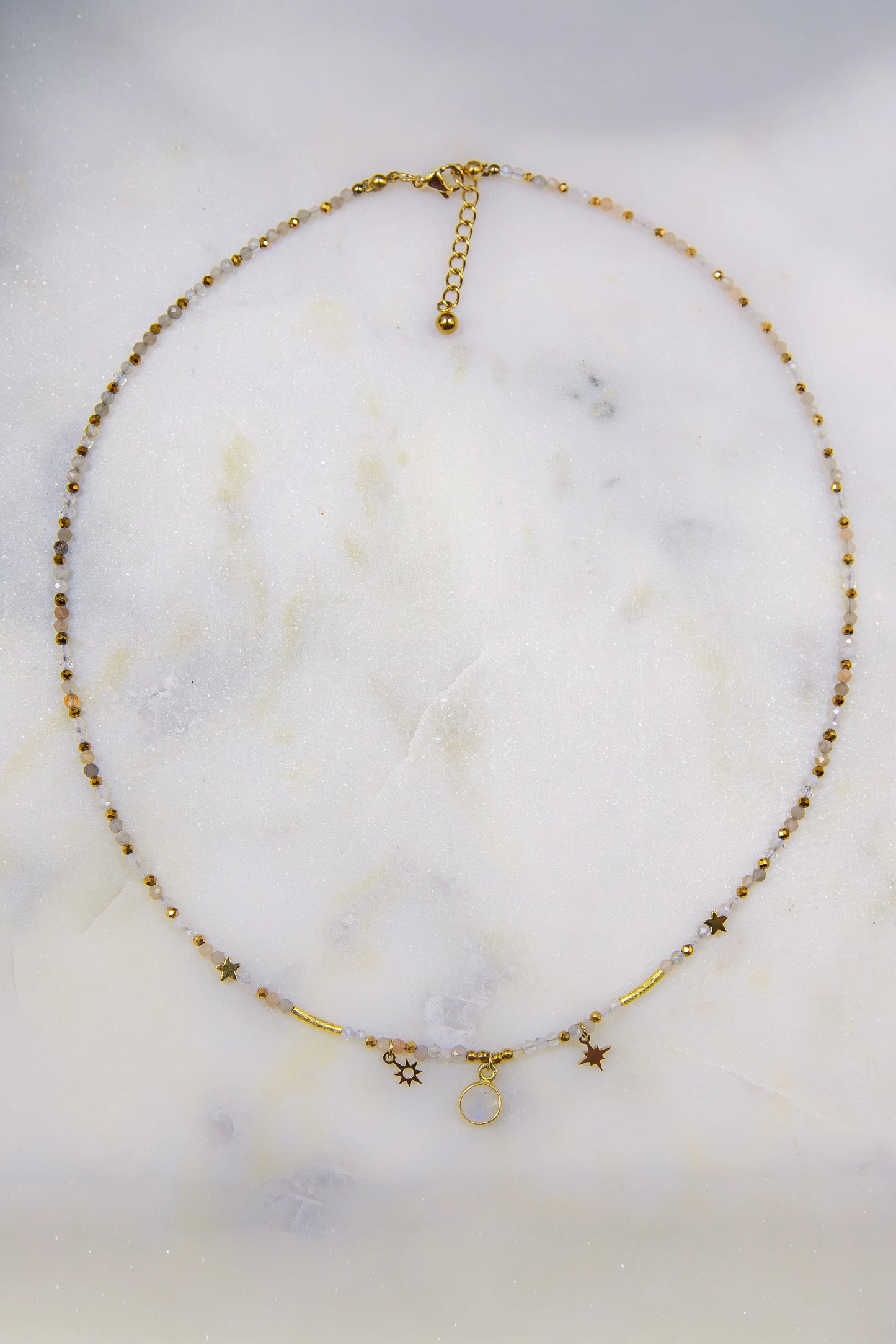 Widok z góry (flat lay) na ręcznie robiony naszyjnik na lince jubilerskiej. Ukazuje harmonijną sekwencję naturalnych minerałów: cytrynu, kamienia słonecznego i jadeitu ze złotymi akcentami i zapięciem.