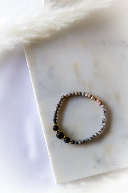 Różane Ognisko Bransoletka Rodonit Lawa ze złotymi przekładkami, o matowym wykończeniu. Ułożona na białym marmurze z delikatnym pióropuszem.