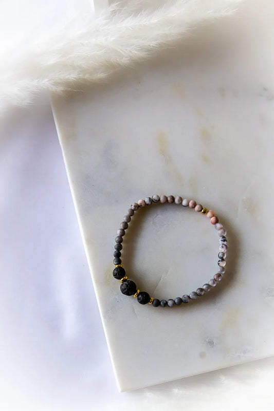 Różane Ognisko Bransoletka Rodonit Lawa ze złotymi przekładkami, o matowym wykończeniu. Ułożona na białym marmurze z delikatnym pióropuszem.