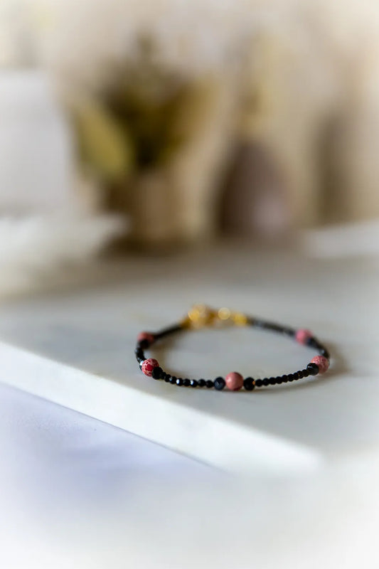 Różowa Ochrona Bransoletka Turmalin Jaspis z czarnymi kamieniami i różowymi akcentami na białej powierzchni.