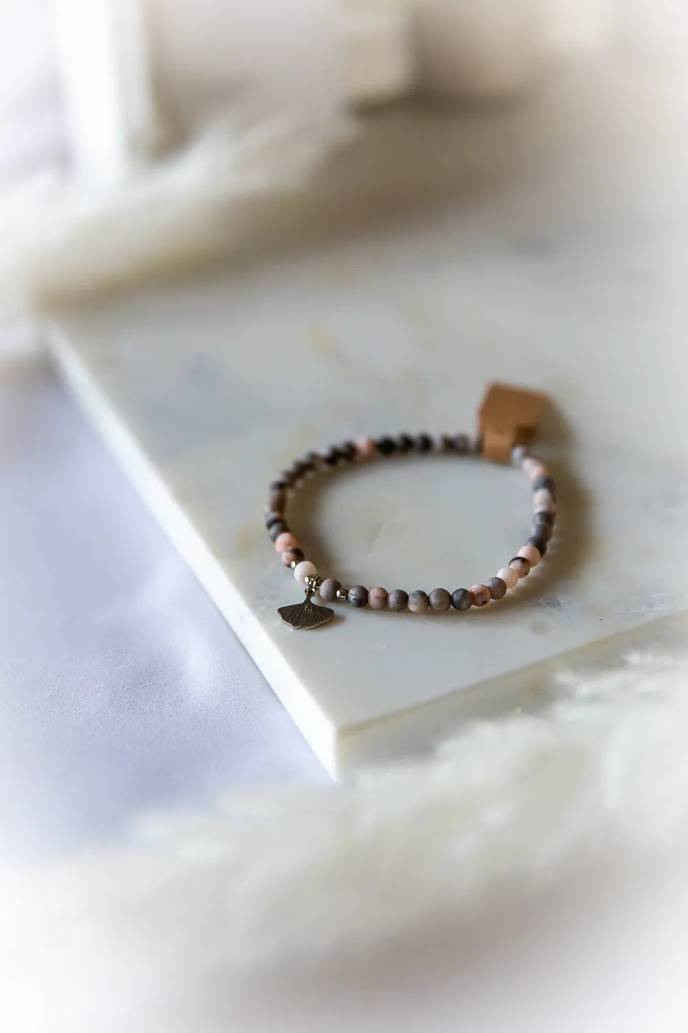 Różowy Zen Bransoletka Rodonit Zawieszka z delikatną srebrną ozdobą w kształcie listka miłorzębu, na marmurowej powierzchni.