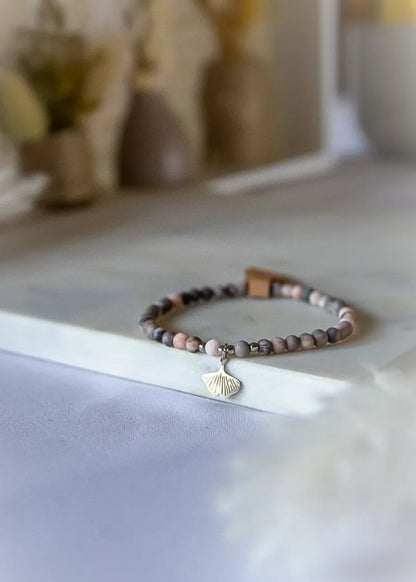 Różowy Zen Bransoletka Z Rodonitu ze srebrną zawieszką w kształcie liścia miłorzębu, na kamiennym tle z subtelnym rozmyciem.