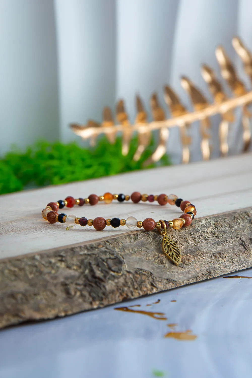 Bransoletka 'SERCE JESIENI' z karneolu, granatu i cytrynu, ułożona na drewnianym pomoście z zielonym mchem w tle i złotym liściem.