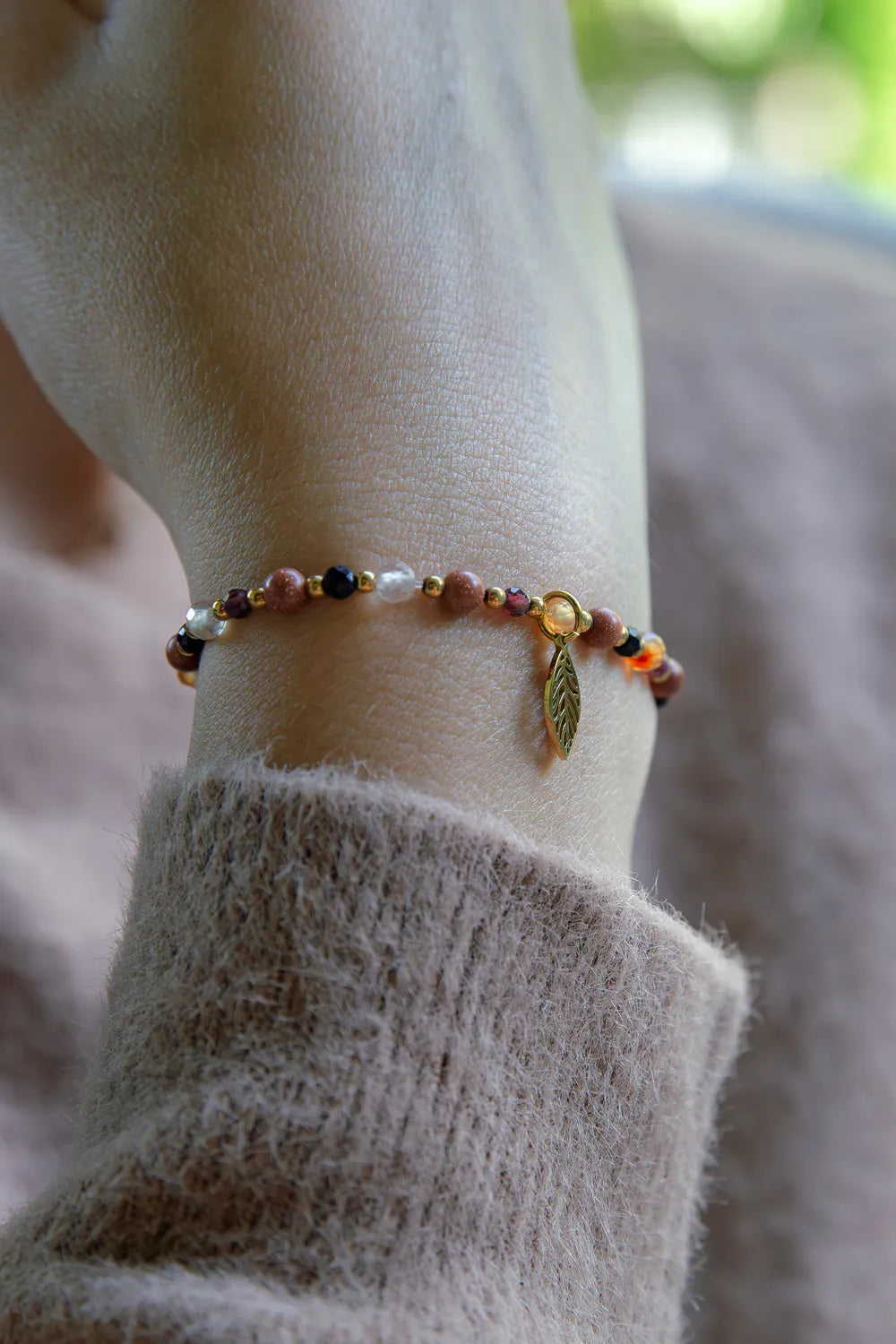 SERCE JESIENI - BRANSOLETKA Z KARNEOLU, GRANATU I CYTRYNU na nadgarstku, z widocznymi kolorowymi kamieniami i złotym liściem, na tle miękkiego, beżowego swetra.
