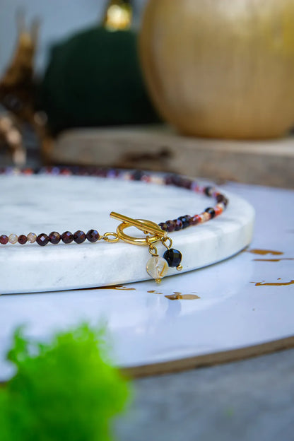 SERCE KRÓLOWEJ - NASZYJNIK Z GRANATU, SPINELU I CYTRYNU, elegancki naszyjnik z kolorowymi kamieniami, ułożony na białym tle z dekoracją w tle.