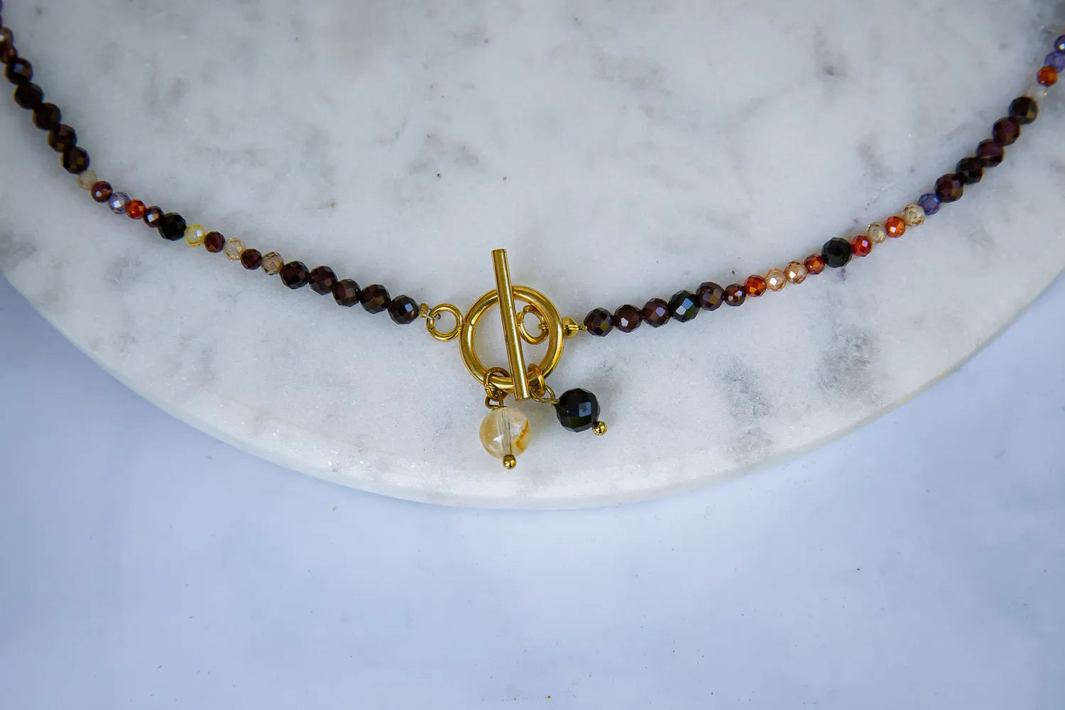 SERCE KRÓLOWEJ - NASZYJNIK Z GRANATU, SPINELU I CYTRYNU, elegancki naszyjnik z kolorowymi kamieniami, ułożony na białym tle z dekoracją w tle.