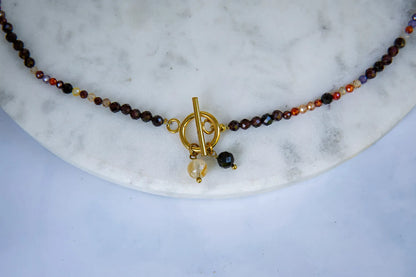 SERCE KRÓLOWEJ - NASZYJNIK Z GRANATU, SPINELU I CYTRYNU, elegancki naszyjnik z kolorowymi kamieniami, ułożony na białym tle z dekoracją w tle.