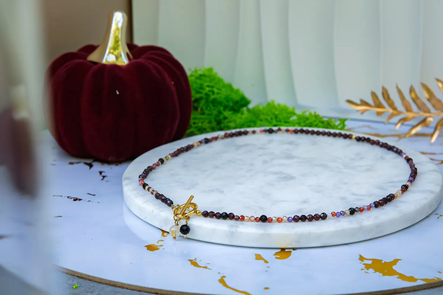 SERCE KRÓLOWEJ - NASZYJNIK Z GRANATU, SPINELU I CYTRYNU. Naszyjnik z kolorowymi kamieniami na marmurowym tle, z czerwoną dynią i zielonym mchem w tle.