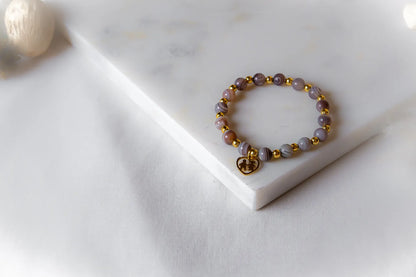 Serce Rodziny Bransoletka Agat Złoto z błyszczącym złotym zawieszką w kształcie serca, na tle białej tkaniny i marmuru.