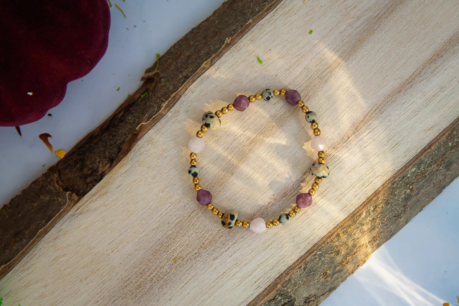 SŁODKI IMPULS - BRANSOLETKA Z JASPISU DALMATYŃSKIEGO I JADEITU. Bransoletka z kolorowymi kamieniami jaspisu dalmatyńskiego i jadeitu, ułożona na drewnianym tle.