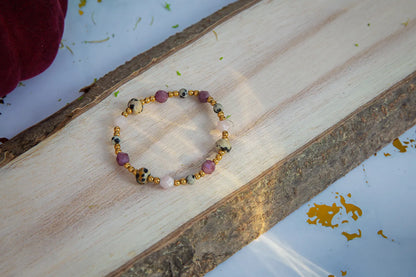 SŁODKI IMPULS - BRANSOLETKA Z JASPISU DALMATYŃSKIEGO I JADEITU. Bransoletka z kolorowymi kamieniami jaspisu dalmatyńskiego i jadeitu, ułożona na drewnianym tle z naturalnymi wzorami.