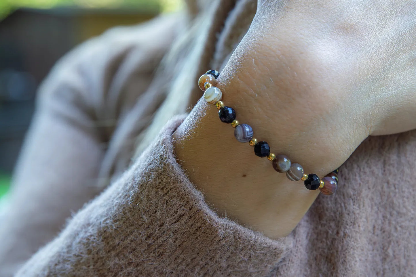 Bransoletka 'STRAŻNIK ENERGII - BRANSOLETKA Z TURMALINU I AGATU BOTSWANA' z widocznymi kolistymi kamieniami turmalinu i agatu botswana, noszona na nadgarstku na tle delikatnej, beżowej bluzy.