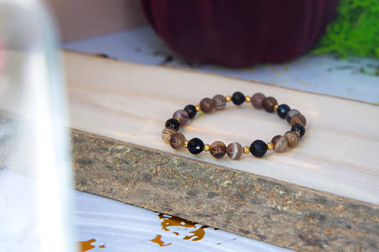 STRAŻNIK ENERGII - BRANSOLETKA Z TURMALINU I AGATU BOTSWANA, złożona z kolorowych koralików turmalinu i agatu, leżąca na drewnianym bloku z naturalnym tłem.