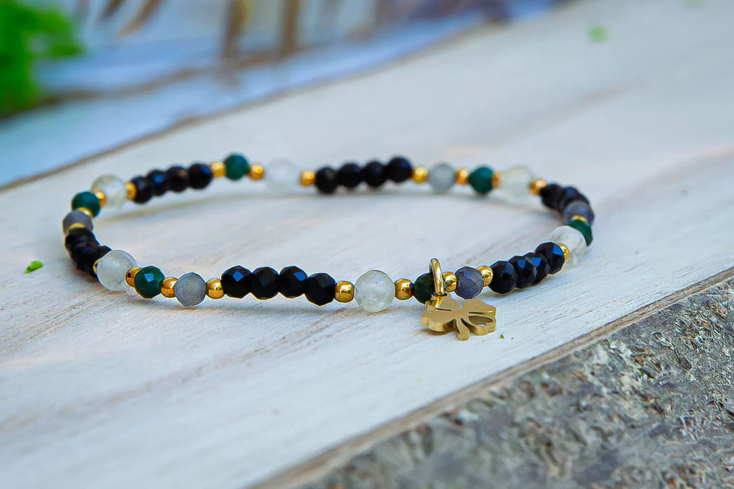 SZEPT SZMARAGDOWEJ WYSPY - BRANSOLETKA Z LEPIDOLITU, CYTRYNU I LABRADORYTU. Zbliżenie na fasetowane kamienie i pozłacaną zawieszkę w kształcie koniczyny, symbolu szczęścia.