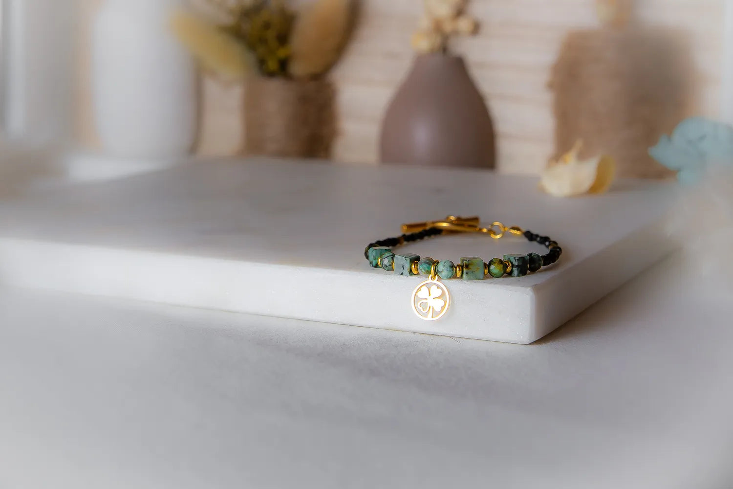 Szczęśliwa Koniczynka Bransoletka Z Turmalinu Czarnego I Turkusu Afrykańskiego Biustonosz z zawieszką koniczynką na tle dekoracji.